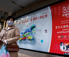 Mujer parada cerca de un anuncio de Alibaba que promociona el festival de compras del Día de los Solteros