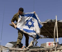 Un soldado israelí cuelga una bandera en un vehículo blindado de transporte de tropas cerca de la frontera con la Franja de Gaza