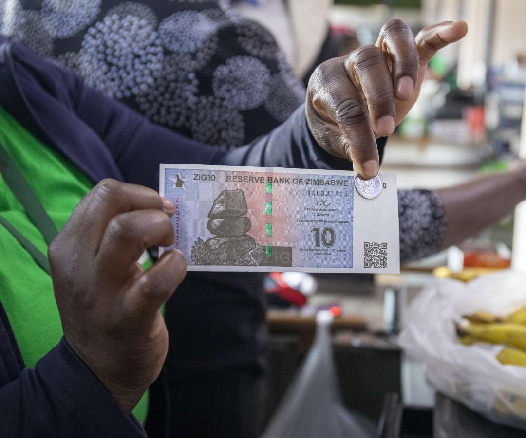 Una cajera de supermercado muestra un billete de 10 ZiG y una moneda de 5 Zig en Harare, Zimbabue