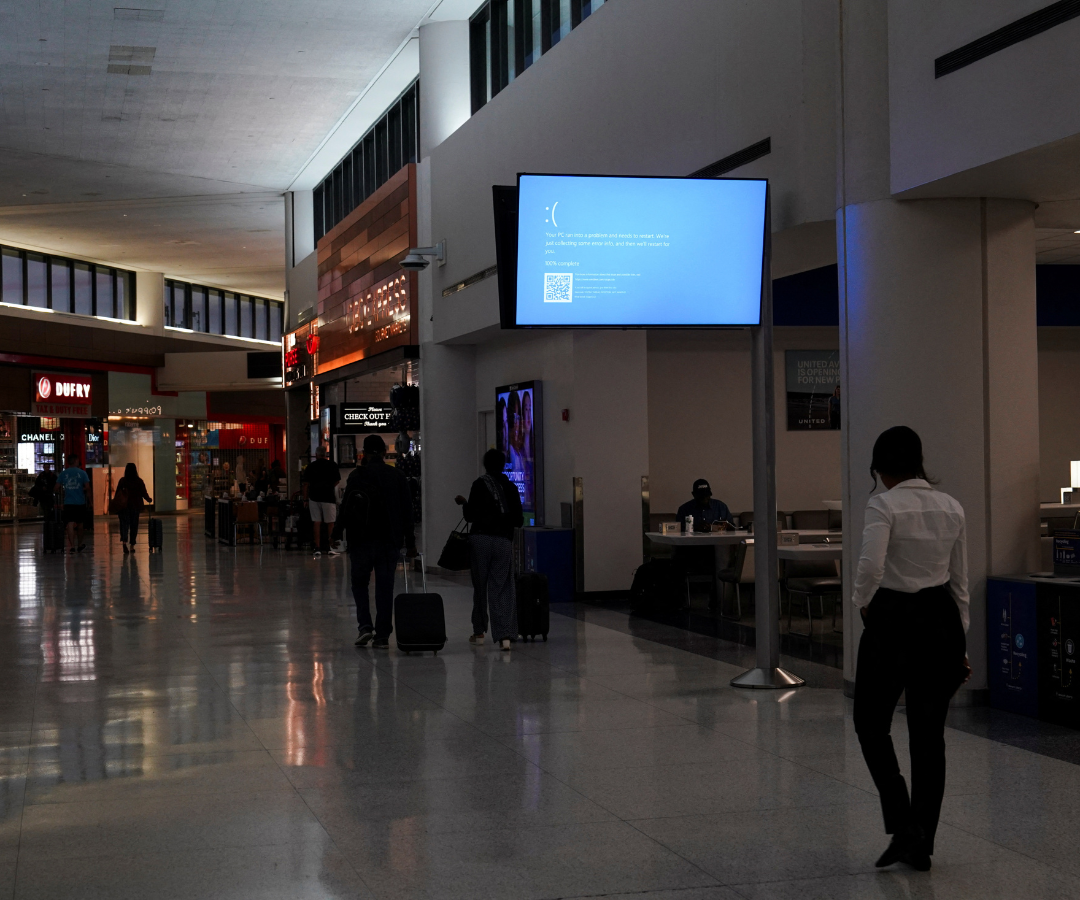 Viajeros y trabajadores del aeropuerto caminan junto a un monitor que muestra una pantalla azul de error, también conocida como la «Pantalla Azul de la Muerte», dentro de la Terminal C del Aeropuerto Internacional de Newark.