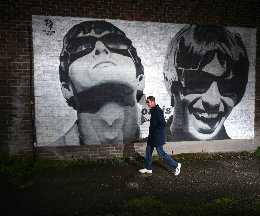 Un aficionado camina frente a un arte de la banda Oasis en la calle