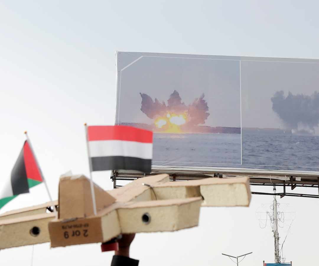 Un manifestante levanta un dron simulado con banderas de Yemen y Palestina bajo una valla publicitaria que muestra un barco atacado por las fuerzas Houthi en el Mar Rojo, durante una manifestación en Hudaydah el 26 de julio.